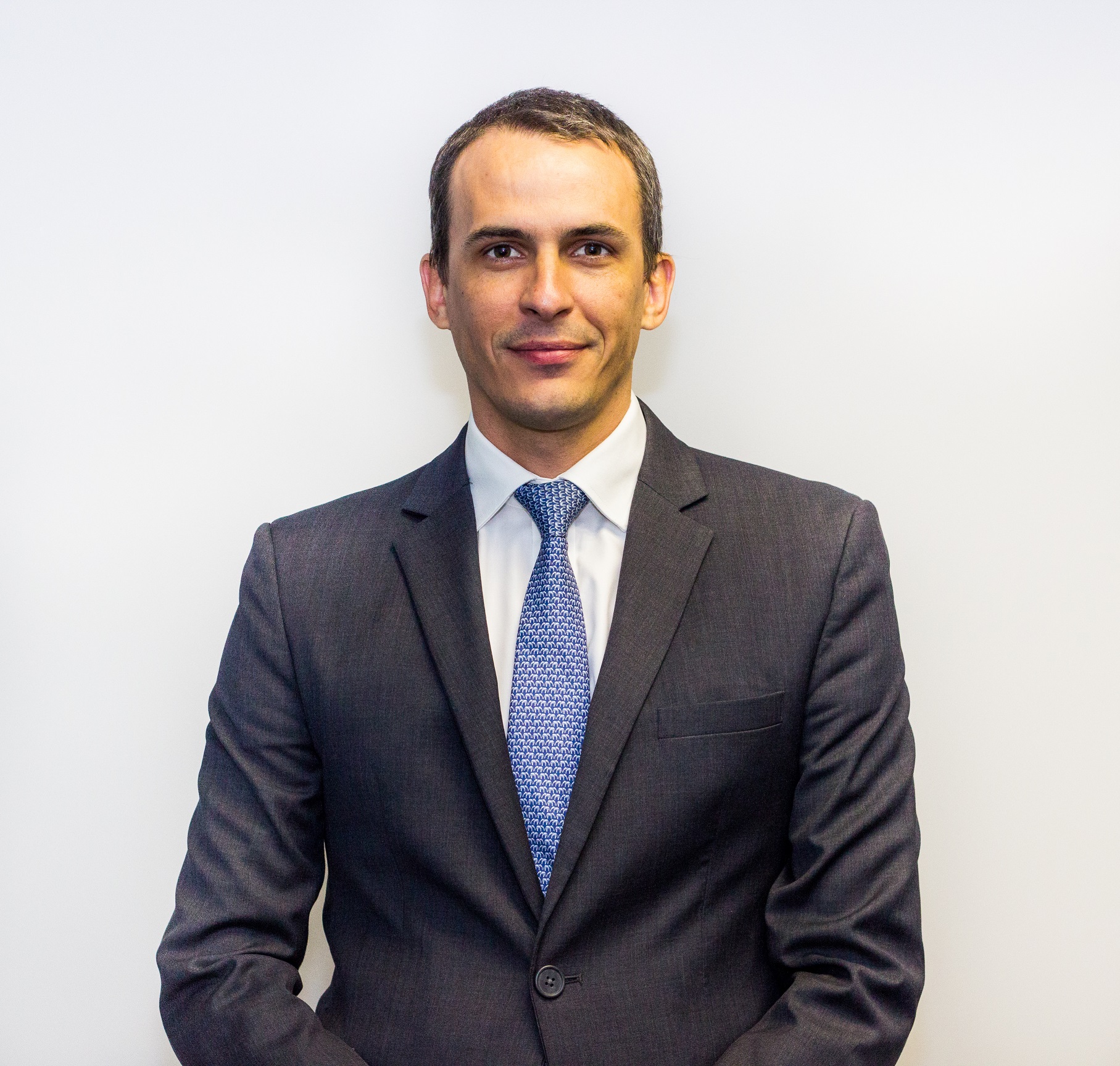 Person in a dark suit with a blue tie standing against a white background.