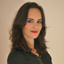 Personne avec des cheveux foncés et rouge à lèvres rouge souriant doucement.