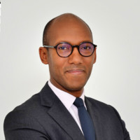Personne en costume et lunettes souriant légèrement.