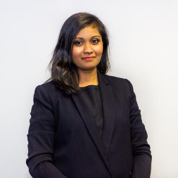 Person in a black suit standing against a white background.