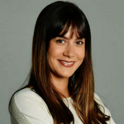 Person smiling warmly with long hair and bangs.