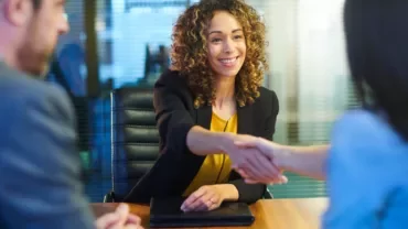 Three people in a meeting room, one person smiling and shaking hands with another.