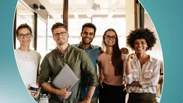 A group of people standing together, smiling in an office setting.