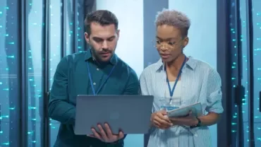 Two people working in a data center, looking at a laptop.