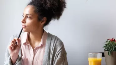 Person sitting at a table with a pen, looking thoughtful.