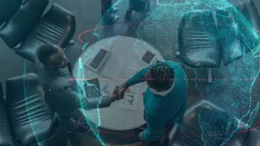 Top view of two people shaking hands over a table with digital globe overlay.