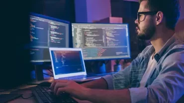 Person programming with multiple screens displaying code.