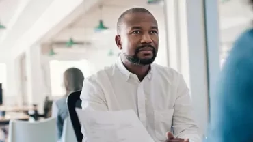 Person holding a document during a meeting in an office setting.