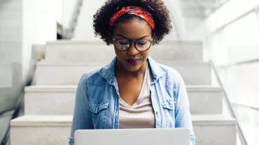 Person sitting on stairs with a laptop and wearing glasses.