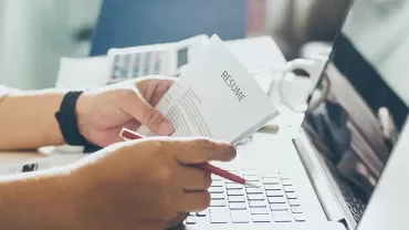 Person reviewing a resume at a desk with a laptop.
