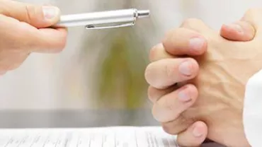 Two people at a table with a document, one holding a pen.