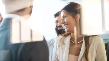 Group of people smiling during a meeting with sticky notes on a window.