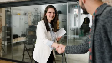 Two people shaking hands in a modern office setting.