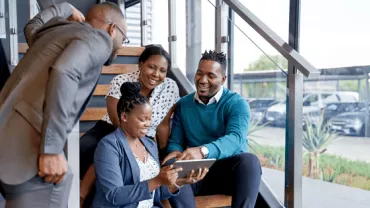 Group of people sitting on stairs looking at a tablet.