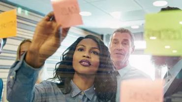People brainstorming with sticky notes on a glass wall.