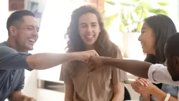 Group of friends smiling and fist bumping around a table.