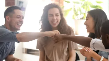 Group of friends smiling and fist bumping around a table.