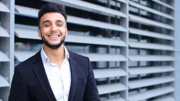 Person smiling in front of modern architectural background.