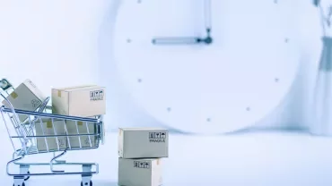 Small shopping cart with boxes, large clock in background.