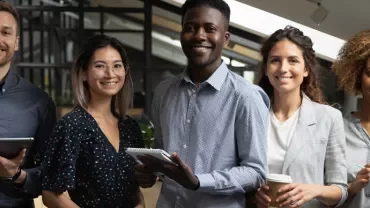 Team of five people smiling in an office setting.