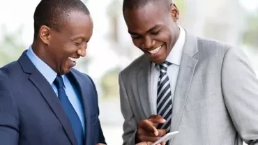 Two people in business attire smiling and looking at a phone.