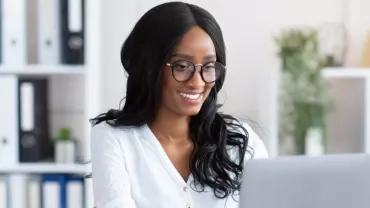 Person smiling while working on a laptop in an office.