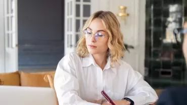 Person wearing glasses working on a laptop in a cozy office.