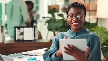 A smilingwoman standing in an office on an ipad 