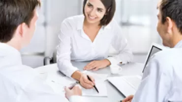 Three people having a meeting at a desk with documents and a laptop.
