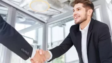 Person in a suit smiling, shaking hands in a modern office.