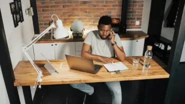 Person on the phone at a wooden desk with a laptop and notebook.