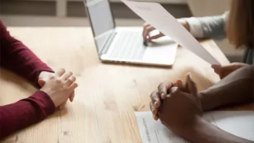 People in a meeting, one with a laptop and paperwork.
