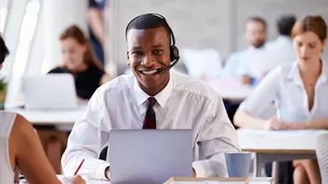 Person wearing headset in an office, working on a laptop.