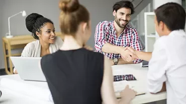 People in a meeting shaking hands around a table, smiling.