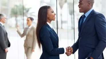 Two people shaking hands in a modern office setting.