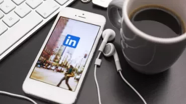 Smartphone with LinkedIn app on screen next to a keyboard and coffee cup.