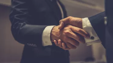 Two people in suits shaking hands indoors.