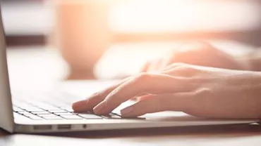 Hands typing on a laptop keyboard in soft lighting.