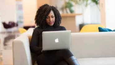 Person sitting on a sofa with a laptop in a bright room.