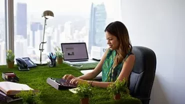 Person working at a desk covered in grass with a city view in the background.