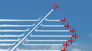 Red planes in formation, one breaking away, leaving white smoke trails against a blue sky.