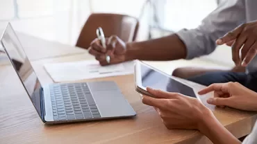 People working together with a laptop and tablet at a desk.