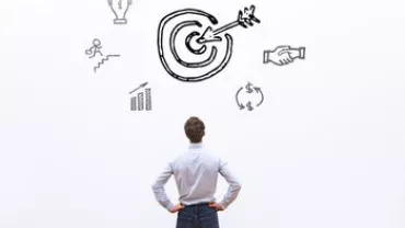Person facing a wall with drawings of a target and various symbols representing goals and success.
