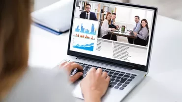Video conference on laptop with charts and meeting participants.