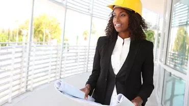 Person wearing a hard hat holding blueprints in a modern building.