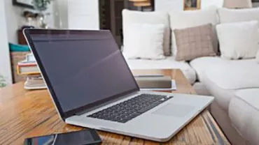 Laptop and smartphone on a wooden coffee table in a living room.