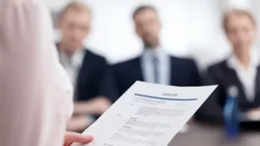 Person holding a resume in front of interview panel.