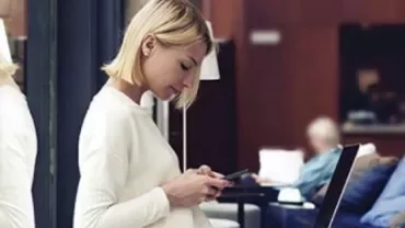 Person using a smartphone next to a laptop in a lounge.