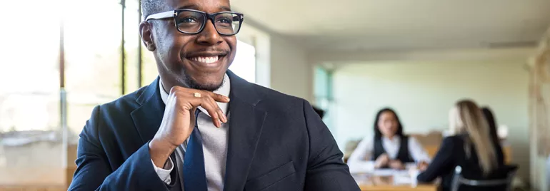 Person in a suit smiling in an office setting.