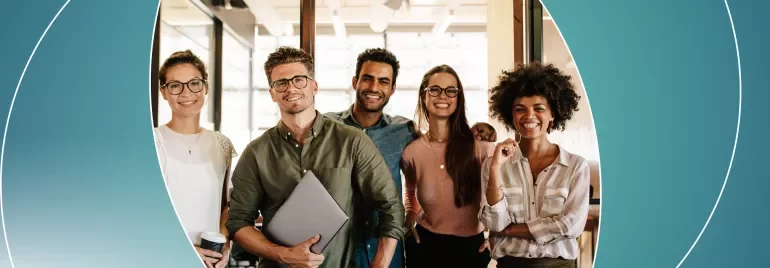 A group of people standing together, smiling in an office setting.